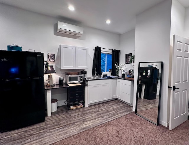 kitchen featuring black refrigerator, a wall unit AC, dark wood-type flooring, sink, and white cabinets