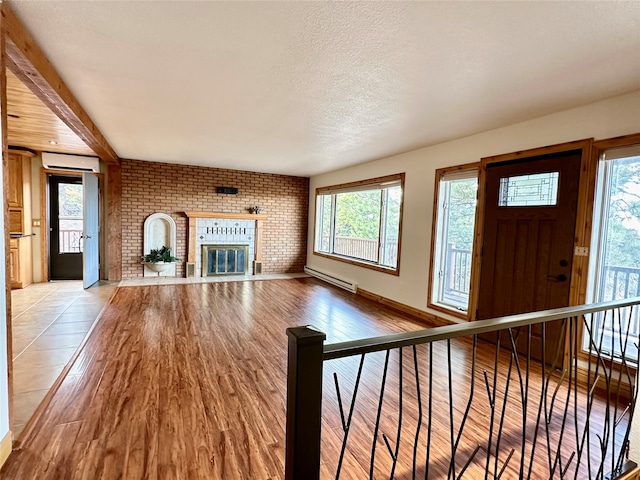 unfurnished living room with a textured ceiling, a baseboard heating unit, a wall unit AC, a brick fireplace, and light hardwood / wood-style flooring