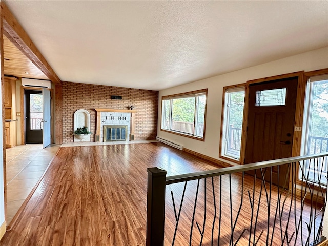 unfurnished living room featuring a textured ceiling, brick wall, a fireplace, a baseboard radiator, and light wood finished floors