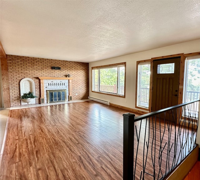 unfurnished living room featuring hardwood / wood-style flooring, baseboard heating, a textured ceiling, and a fireplace