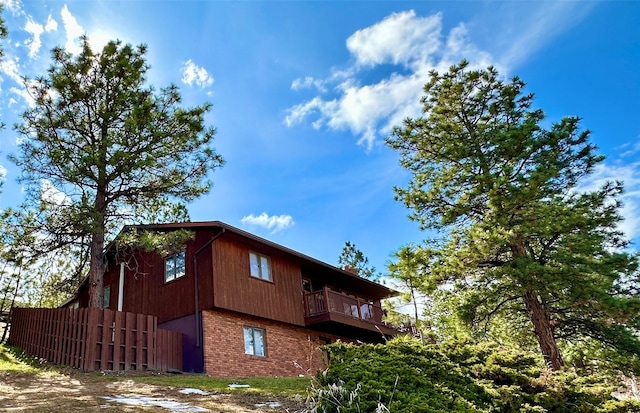 view of side of home featuring brick siding, fence, and a balcony