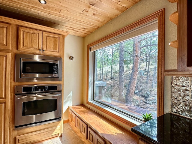 kitchen with tile patterned floors, brown cabinets, wooden ceiling, dark stone countertops, and appliances with stainless steel finishes