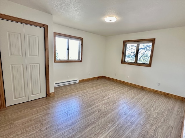 unfurnished bedroom with a baseboard heating unit, a closet, a textured ceiling, and light hardwood / wood-style flooring