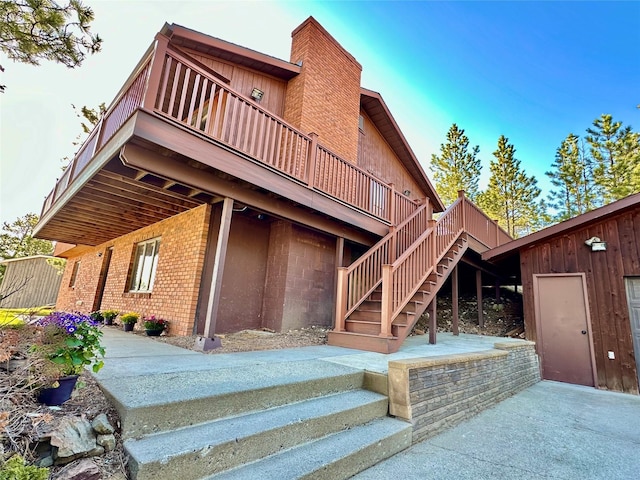 rear view of house featuring stairs, a wooden deck, and a chimney