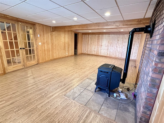 basement with a drop ceiling, wood walls, a wood stove, and wood-type flooring