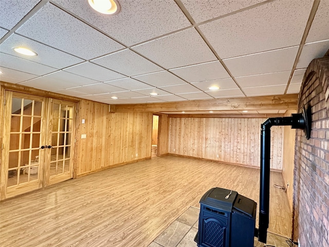 basement with wood-type flooring, a wood stove, a drop ceiling, and wooden walls