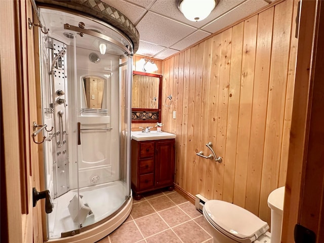 full bathroom featuring a stall shower, tile patterned floors, a baseboard heating unit, toilet, and wooden walls