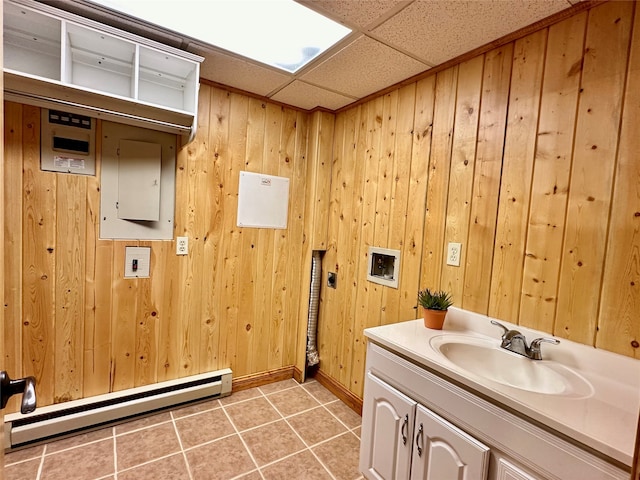 bathroom with a paneled ceiling, wood walls, and a baseboard radiator