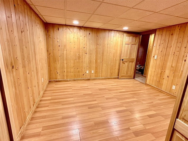 empty room featuring a paneled ceiling, wooden walls, and light wood-style flooring