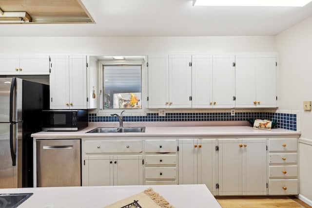 kitchen featuring sink, light hardwood / wood-style flooring, decorative backsplash, appliances with stainless steel finishes, and white cabinetry