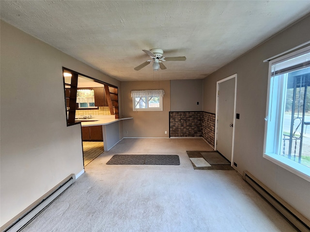 interior space featuring ceiling fan, brick wall, baseboard heating, and light colored carpet