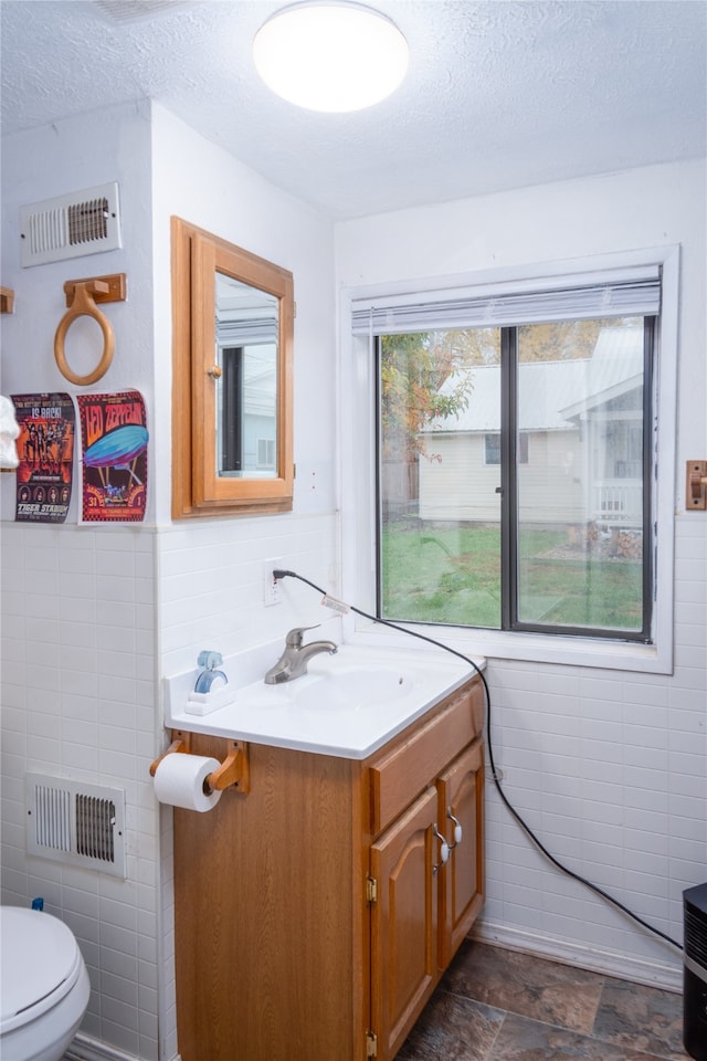 bathroom featuring vanity, toilet, tile walls, and a textured ceiling