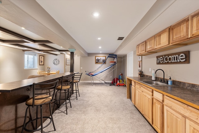 kitchen with sink, light carpet, beamed ceiling, a breakfast bar area, and light brown cabinets