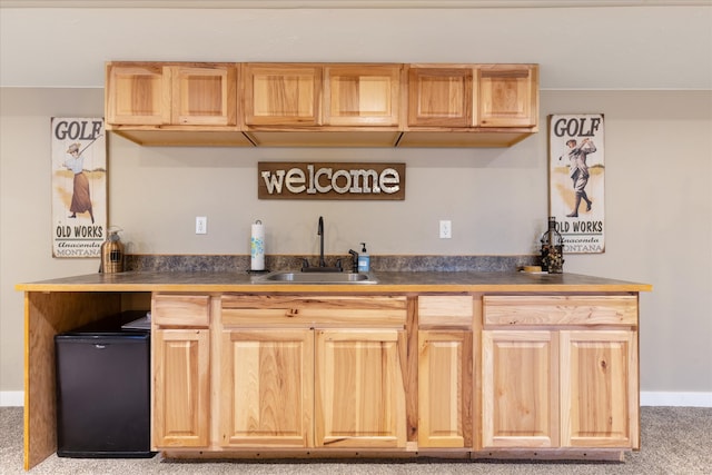 kitchen with sink, light brown cabinets, light carpet, and black fridge