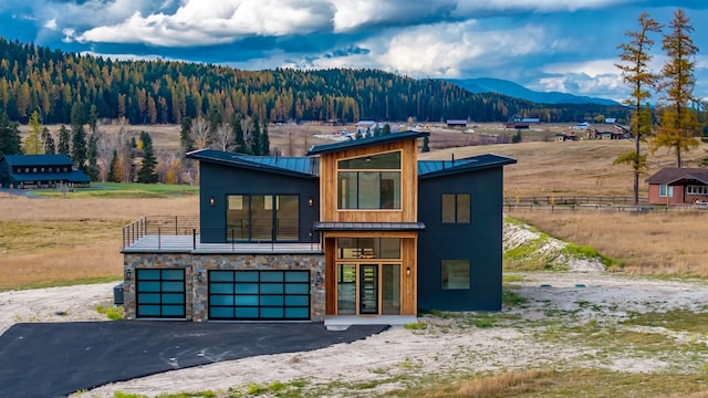 contemporary home with metal roof, a balcony, stone siding, driveway, and a standing seam roof