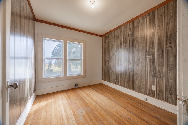 empty room with ornamental molding, wooden walls, and light hardwood / wood-style floors