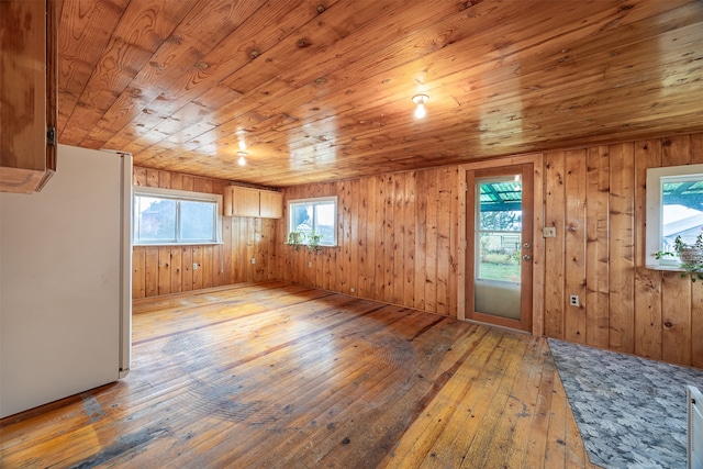 unfurnished living room featuring wooden walls, wooden ceiling, light hardwood / wood-style flooring, and plenty of natural light