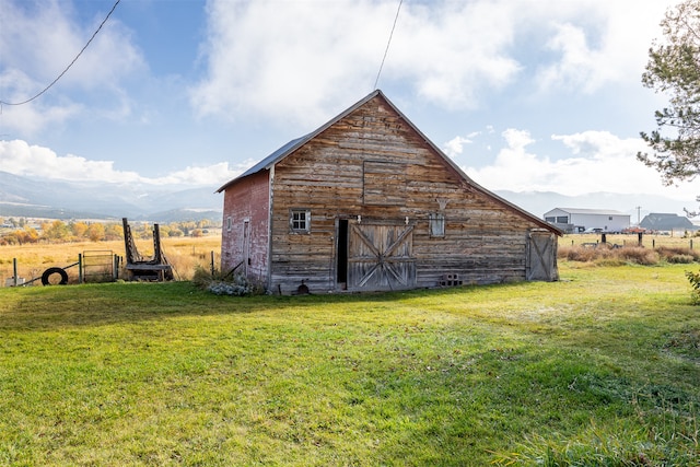 view of outbuilding featuring a rural view, a yard, and a mountain view