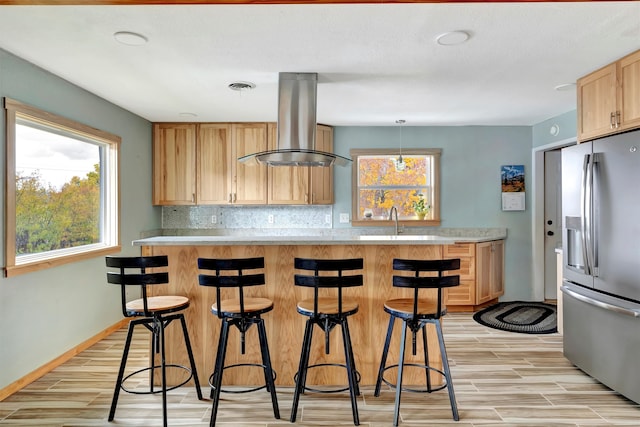 kitchen with light hardwood / wood-style flooring, backsplash, island exhaust hood, stainless steel fridge, and pendant lighting