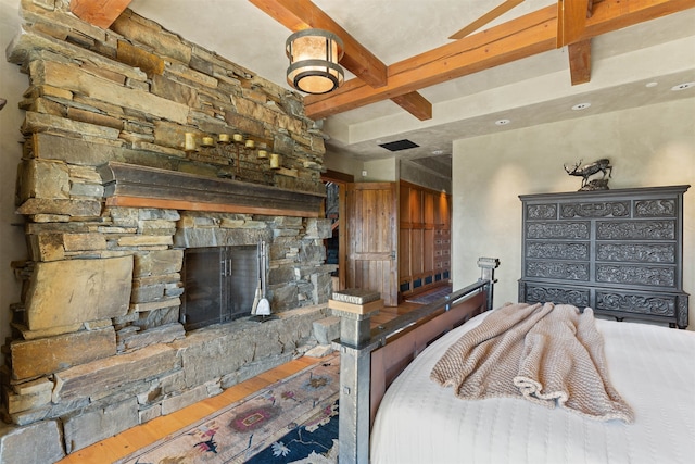 bedroom featuring beamed ceiling, hardwood / wood-style floors, and a fireplace