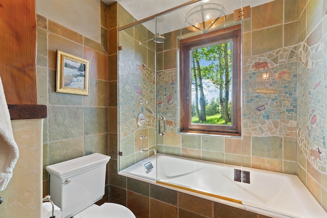 bathroom with toilet, tile walls, and bath / shower combo with glass door