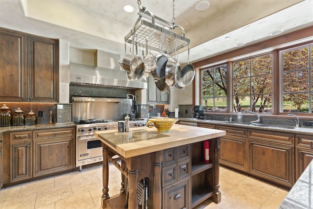 kitchen with tasteful backsplash, light stone countertops, luxury stove, and ventilation hood