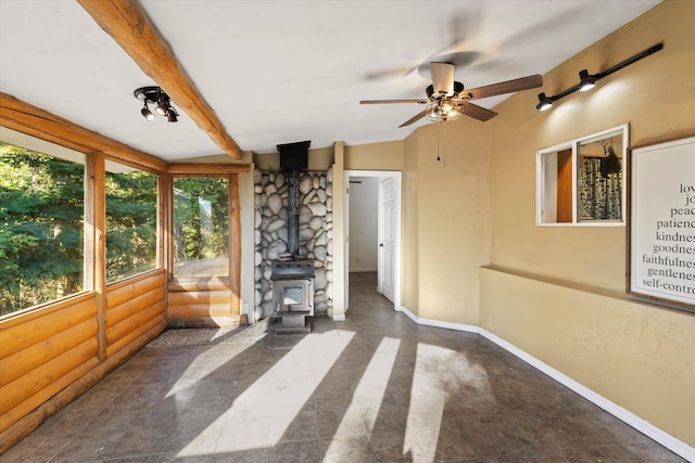 unfurnished sunroom featuring ceiling fan, a wood stove, and beamed ceiling