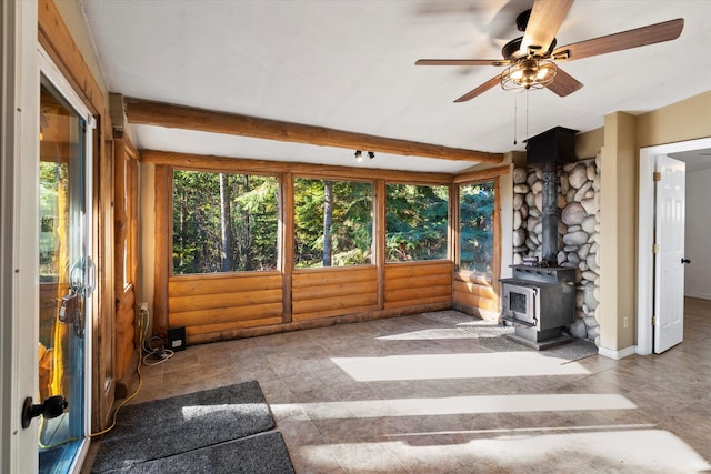 unfurnished sunroom with a wood stove, beamed ceiling, and ceiling fan