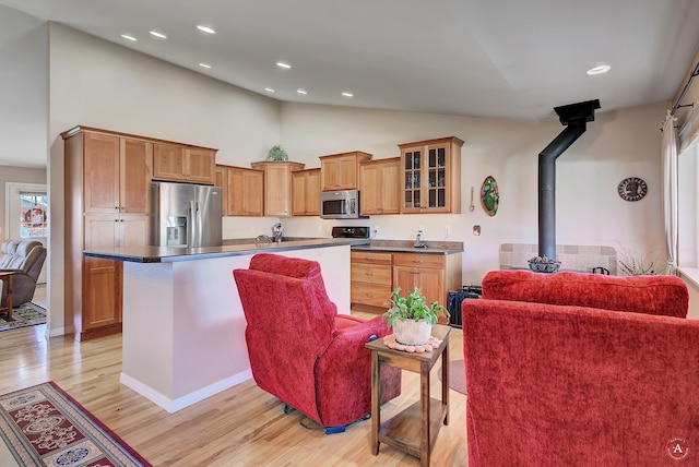 kitchen featuring appliances with stainless steel finishes, a wood stove, high vaulted ceiling, and light wood-type flooring