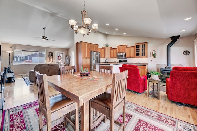 dining area featuring lofted ceiling, ceiling fan with notable chandelier, light wood-type flooring, and a wood stove