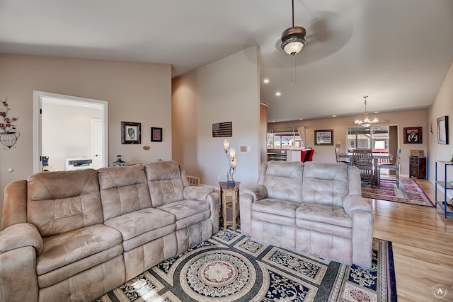 living room featuring light hardwood / wood-style flooring, ceiling fan with notable chandelier, and vaulted ceiling