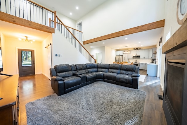 living room with beamed ceiling, a high ceiling, a chandelier, and hardwood / wood-style floors