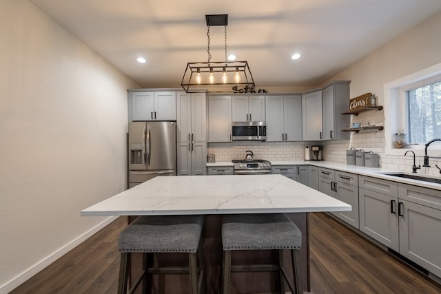 kitchen with appliances with stainless steel finishes, sink, a kitchen island, dark hardwood / wood-style flooring, and pendant lighting