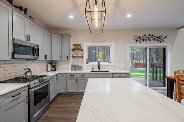 kitchen with appliances with stainless steel finishes, light stone countertops, sink, and dark wood-type flooring