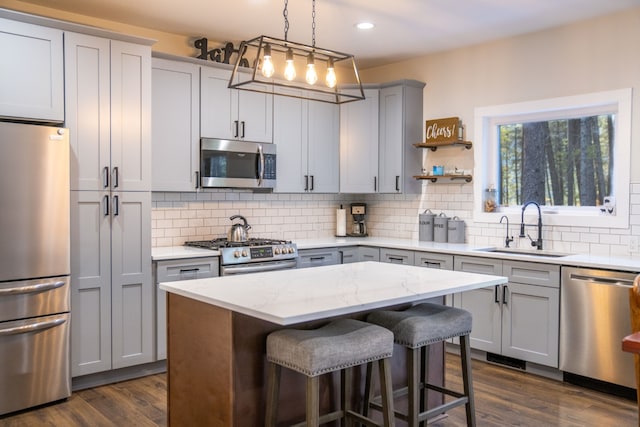 kitchen with light stone counters, stainless steel appliances, dark wood-type flooring, sink, and a center island