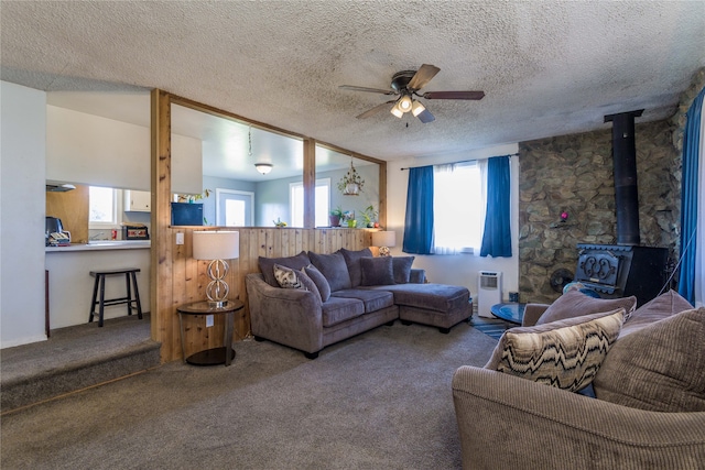 carpeted living room featuring a wood stove, ceiling fan, and a textured ceiling