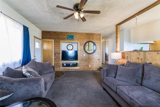 living area featuring carpet floors, a ceiling fan, wood walls, and a textured ceiling