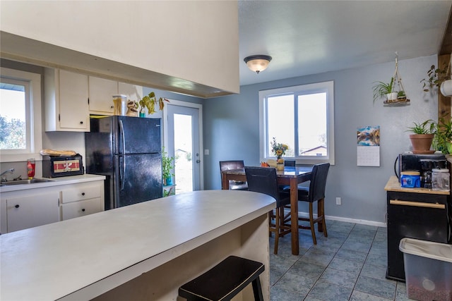 kitchen with white cabinets, a sink, light countertops, freestanding refrigerator, and baseboards