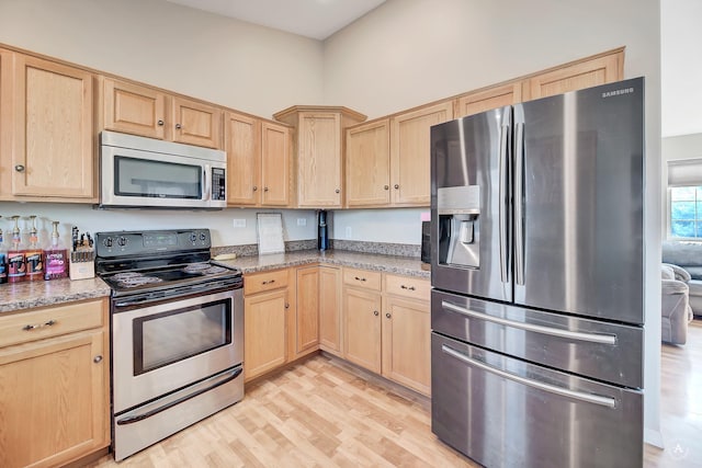 kitchen featuring light brown cabinets, a towering ceiling, light hardwood / wood-style floors, light stone counters, and stainless steel appliances