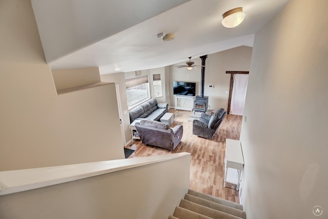 staircase with a wood stove, ceiling fan, wood-type flooring, and lofted ceiling