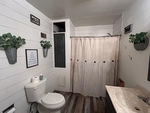 bathroom featuring wood-type flooring, toilet, wooden walls, vanity, and electric panel