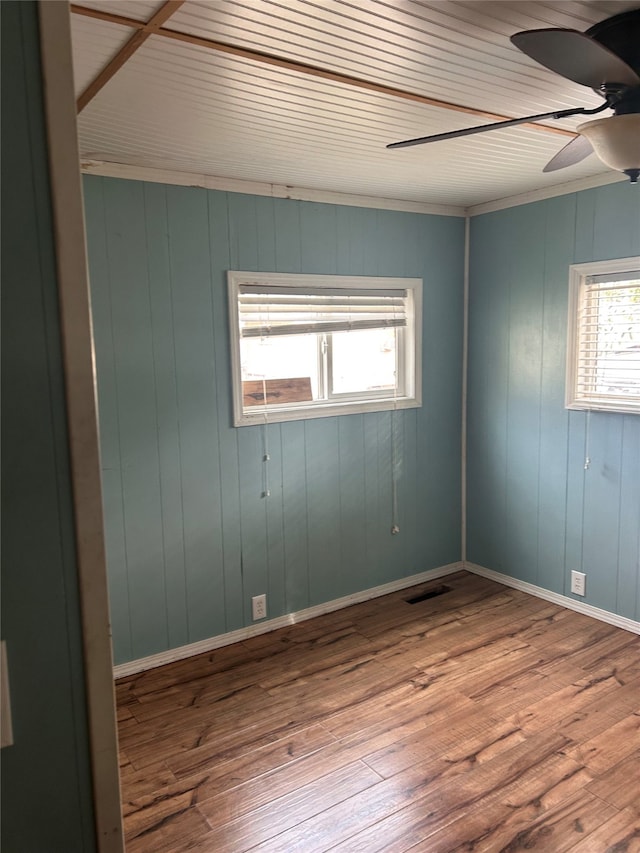 unfurnished room with ornamental molding, wood walls, wood-type flooring, and ceiling fan