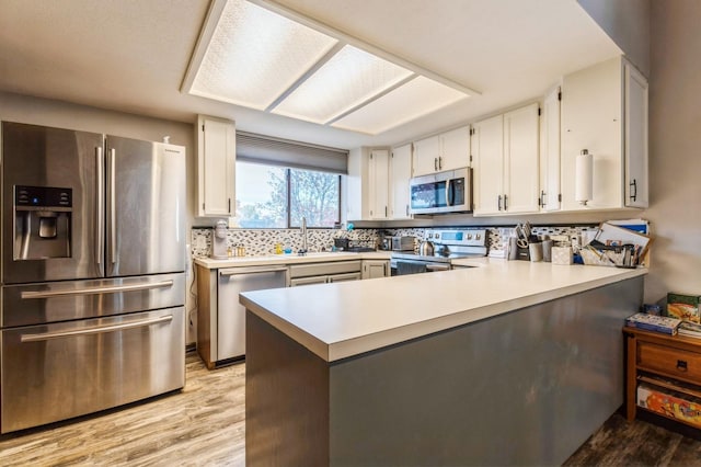 kitchen featuring a peninsula, stainless steel appliances, light countertops, white cabinetry, and a sink