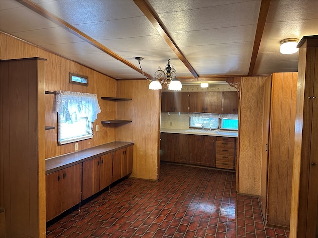 kitchen with decorative backsplash, sink, a notable chandelier, pendant lighting, and wood walls