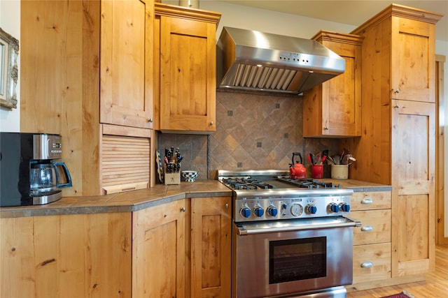 kitchen with wall chimney exhaust hood, light hardwood / wood-style floors, high end stove, and tasteful backsplash