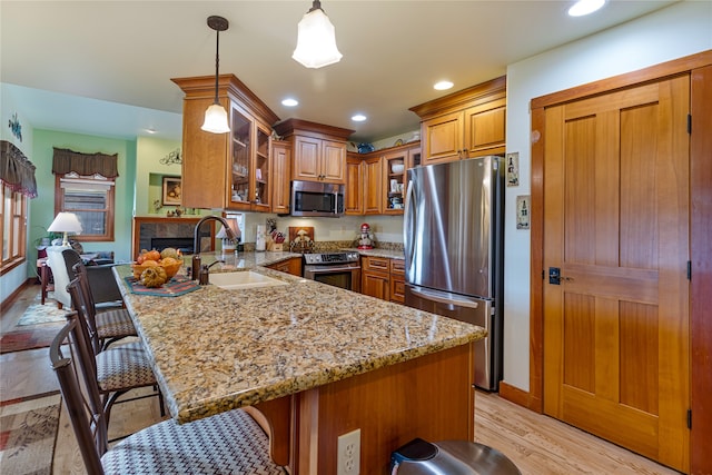 kitchen with sink, kitchen peninsula, light hardwood / wood-style floors, stainless steel appliances, and pendant lighting