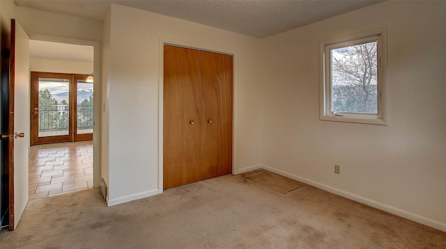 unfurnished bedroom with a textured ceiling, multiple windows, a closet, and light colored carpet