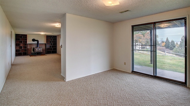 carpeted spare room with a wood stove and a textured ceiling