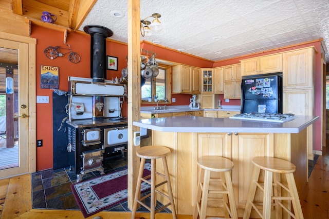 kitchen featuring a breakfast bar, sink, stainless steel gas cooktop, black refrigerator, and light brown cabinetry