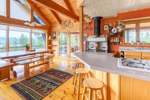 kitchen featuring white gas cooktop, sink, light hardwood / wood-style flooring, vaulted ceiling with beams, and a kitchen bar